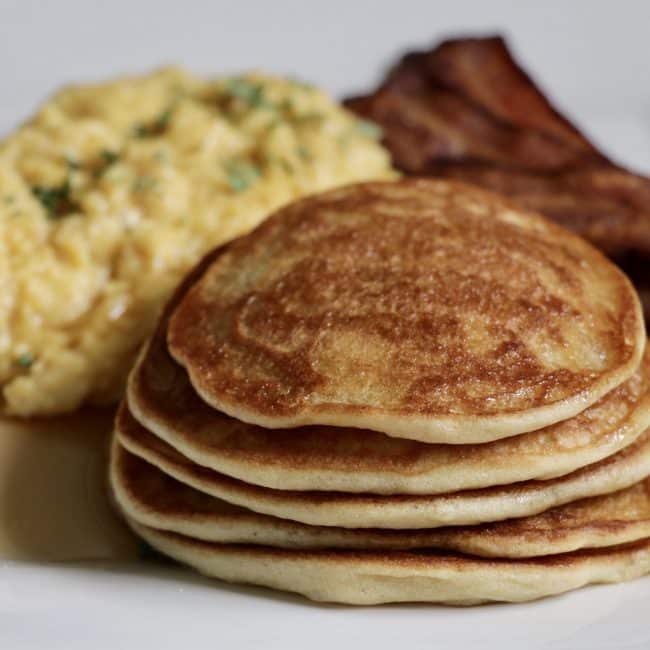 Gluten-Free pancakes with scrambled eggs and bacon on a white plate.