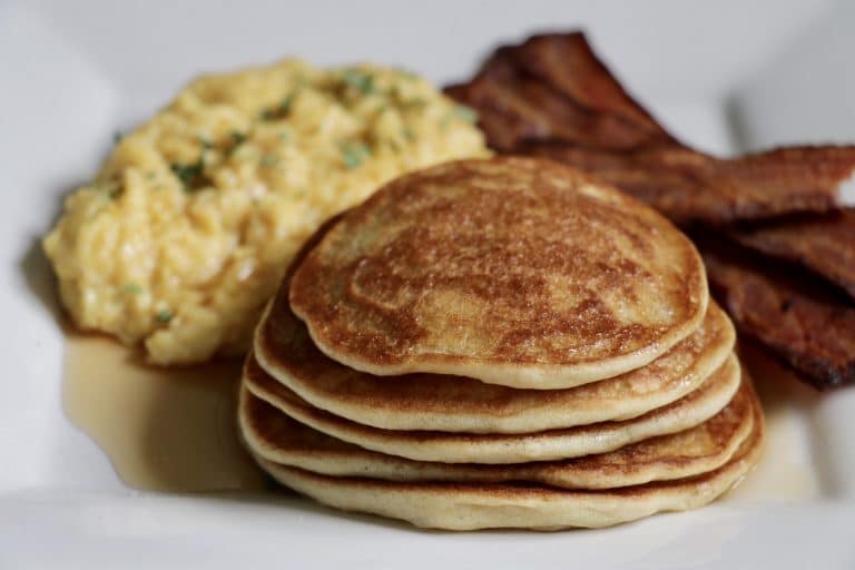 Gluten-Free pancakes with scrambled eggs and bacon on a white plate.